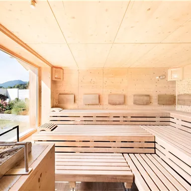 A modern sauna with wooden paneling and large windows. In the background, a peaceful landscape can be seen.