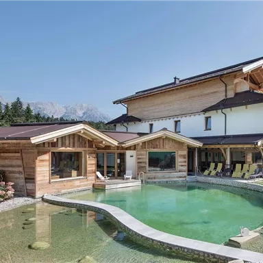A modern chalet architecture with a beautiful, natural pool and a generous garden landscape. Majestic mountains are visible in the background.