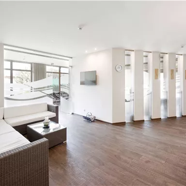 A modern living room with a bright, open space. There is a white couch, wooden flooring, and large windows that let in plenty of light.