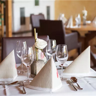 An elegantly set table in the restaurant with white tablecloths and decorative napkins. Glasses and cutlery are carefully arranged, creating an inviting atmosphere.