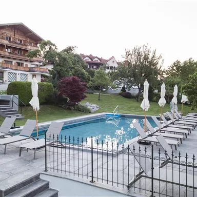 Ein ruhiger Poolbereich mit Liegen und Sonnenschirmen. Umgeben von gepflegten Grünflächen und modernen Gebäuden.