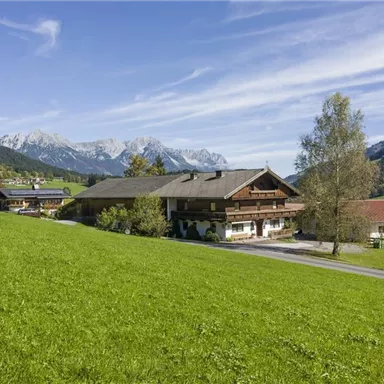 Ein idyllisches Haus in einer grünen Wiese mit Blick auf die Berge. Die Landschaft ist ruhig und malerisch mit blauen Himmel.