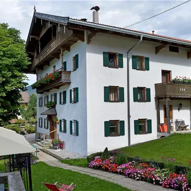 Ein charmantes, dreistöckiges Gebäude mit weißen Wänden und grünen Fensterläden. Der Garten ist mit bunten Blumen und einem Spielplatz ausgestattet.