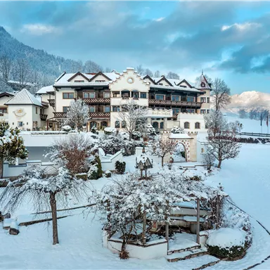An idyllic hotel in the snow, surrounded by snow-covered trees and mountains. The sky is lightly clouded, giving the scene a calm atmosphere.