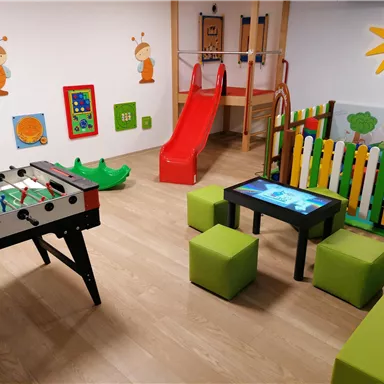 A colorful playroom with a slide, a foosball table, and an interactive table. The walls are decorated with cheerful motifs and colors.