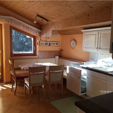 A bright and inviting kitchen with a wooden ceiling and large windows. The dining area is furnished with a table and chairs.