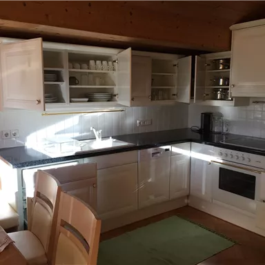 A bright kitchen with white cabinets and modern appliances. A dining table with chairs is located in the foreground.