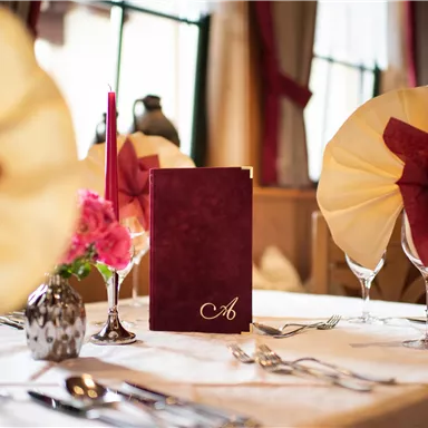 Ein elegant gedeckter Tisch mit einer Speisekarte und stilvollen Servietten. Die Dekoration umfasst Blumen und Kerzen, die eine gemütliche Atmosphäre schaffen.