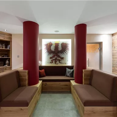 Ein moderner Empfangsbereich mit gemütlichen Sitzgelegenheiten aus Holz und komfortablen Polstern. Im Hintergrund ist ein stilisiertes Wappen mit einem Adler zu sehen.