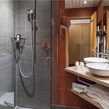 Ein modernes Badezimmer mit einer Glasdusche und zwei Waschbecken. Die Wände sind in beruhigenden Grautönen gestaltet.