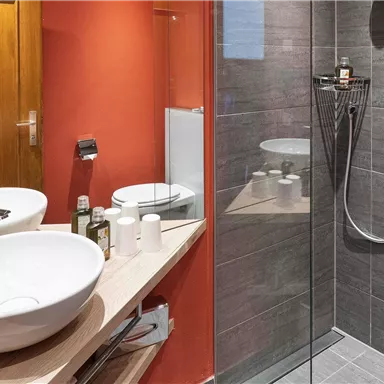 Ein modernes Badezimmer mit einer Dusche und einem großen Waschbecken. Die Wände sind in warmen Farben gehalten und die Ausstattung ist stilvoll und funktional.