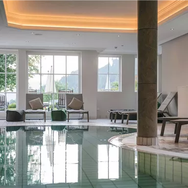 Ein heller Wellnessbereich mit einem Pool und Liegen. Große Fenster sorgen für viel Tageslicht und eine entspannte Atmosphäre.