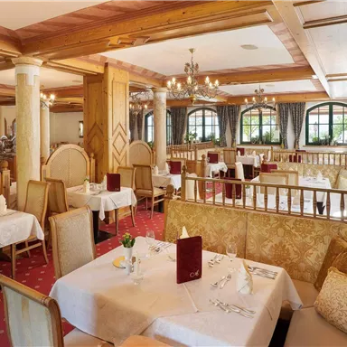 Ein elegantes Restaurant mit Holzelementen und hellen Tischen. Die gemütliche Atmosphäre wird durch große Fenster und stilvolle Beleuchtung ergänzt.