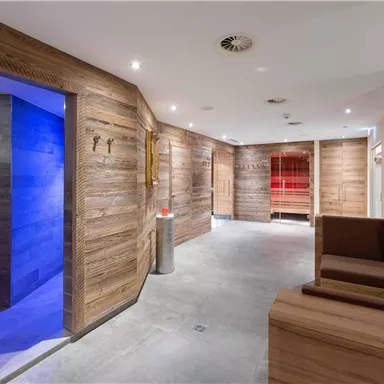 Ein moderner Wellnessbereich mit Holzverkleidungen und entspannendem Ambiente. Im Hintergrund sind Sauna- und Duschbereiche sichtbar.