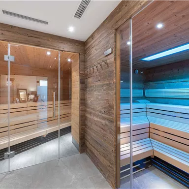 Ein moderner Wellnessbereich mit zwei Saunen aus Holz und Glas. Die Atmosphäre ist entspannend und einladend.