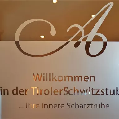 Einflussreiches Schild an einer Glastür. Es begrüßt die Gäste in der "Tiroler Schwitzstube" und weist auf eine entspannende Atmosphäre hin.