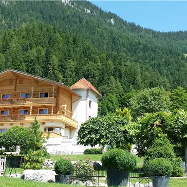 Ein gemütliches Holzhaus inmitten einer grünen Berglandschaft. Der Himmel ist klar und die Umgebung ist üppig bewachsen.