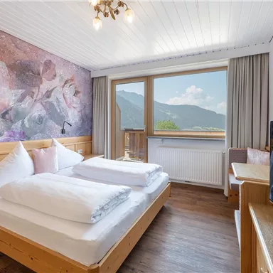 Ein gemütliches Hotelzimmer mit zwei Betten und Holzdekor. Durch das Fenster blickt man auf eine malerische Berglandschaft.