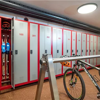 A spacious locker room with many lockers. A bicycle stands next to an open locker, where ski equipment is stored.