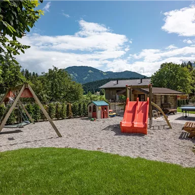 A beautiful playground with a slide and swings. In the background, mountains and a house are visible.