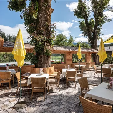 A cozy outdoor restaurant with a wooden terrace and armchairs. Yellow umbrellas provide shade under a blue sky.