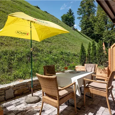 An inviting outdoor area with a table and chairs under a yellow umbrella. In the background, green hills and trees are visible.