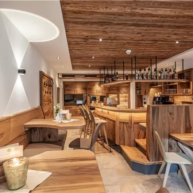 A cozy restaurant with wooden furniture and warm light. The bar counter is clearly visible and the atmosphere is inviting.