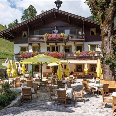 A cozy inn in the mountains with blooming window sills. The terrace is equipped with yellow umbrellas and wooden furniture, perfect for outdoor offerings.
