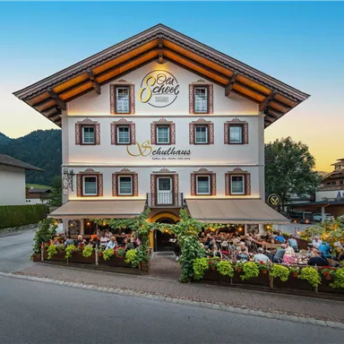 A charming restaurant with a flower-decorated outdoor area. In the background, mountains and a clear sky can be seen.