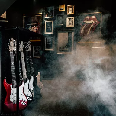A narrow passage with guitars leaning against a wall. The room is enveloped in smoke and decorated with music pictures.