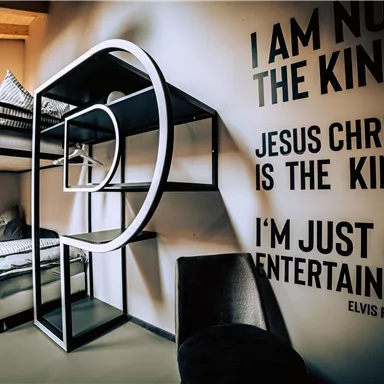 A modern room with a loft bed and a cozy armchair. On the wall are quotes that address the themes of entertainment and identity.