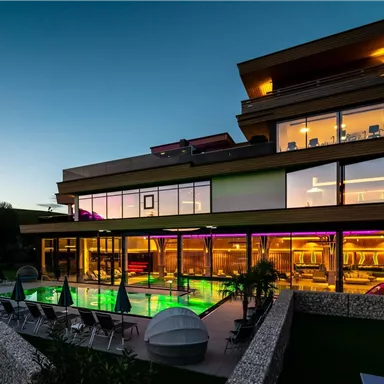 A modern building with large windows and a illuminated pool. The evening atmosphere is calm and welcoming.