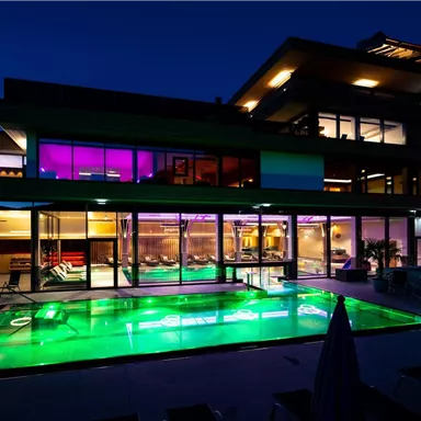 A modern villa with a illuminated outdoor pool. The windows are generous and showcase a stylish interior design.