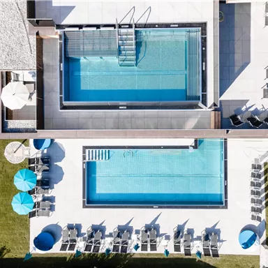 Two swimming pools in a modern complex, surrounded by sunbeds and parasols. The architecture is elegant and inviting.