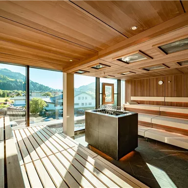 A modern sauna with wooden shelves and large windows. The view of the mountains and the surroundings creates a relaxing atmosphere.