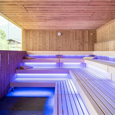 A modern wellness area with wooden paneling and atmospheric blue light. The benches are made of light wood and create a relaxing atmosphere.