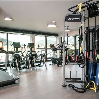 A modern gym with a treadmill and various training equipment. Large windows offer a view of nature.