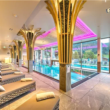 An elegant wellness area with loungers and a large swimming pool. The atmosphere is accented by soft lighting and modern design.