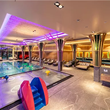 A modern wellness area with a swimming pool, colorful lights, and comfortable loungers. The atmosphere is relaxing and inviting.