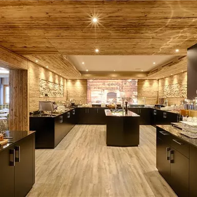 A modern restaurant kitchen with wood paneling and elegant black furniture. There is a buffet with various foods and drinks.