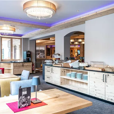 A modern restaurant with wooden furniture and comfortable seating areas. There is a buffet area with dishes and a stylish atmosphere.