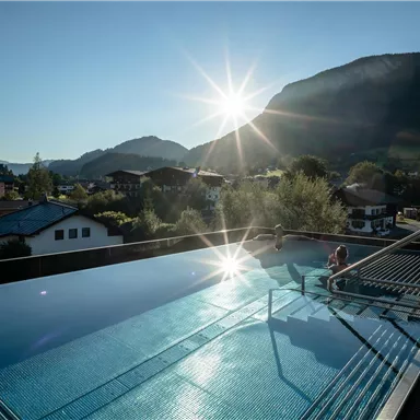 A breathtaking infinity pool with a view of the mountains in the background. The sun is shining brightly and reflecting off the water.