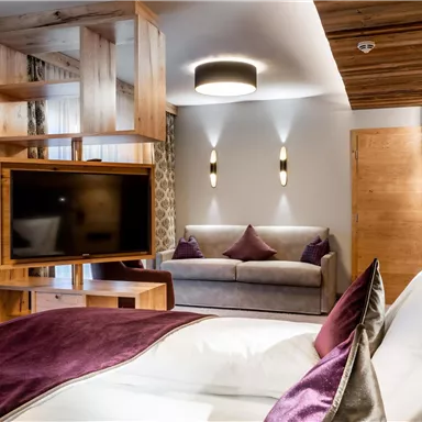 A modern hotel room with a cozy bed and a seating area. The warm wooden tones and elegant decor create an inviting atmosphere.