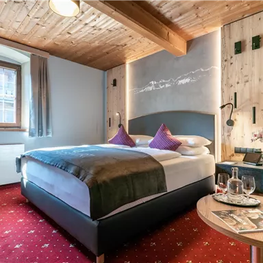 A cozy hotel room with a large bed and subtle wooden decor. The room has large windows and an inviting atmosphere.