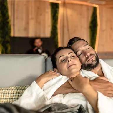 A couple relaxes in a cozy room, embraced and wrapped in fluffy bathrobes. The atmosphere is warm and inviting.
