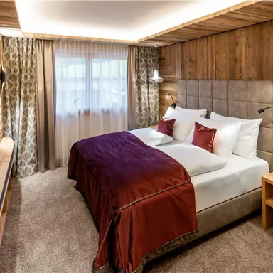 A cozy bedroom with wooden walls and a large bed. Soft textiles and warm light create an inviting atmosphere.