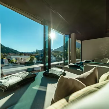 A modern living room with large windows that offer a view of the mountains.  
Bright sunlight and cozy seating invite you to relax.