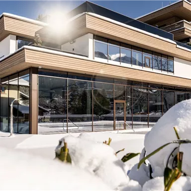 A modern building with large windows, surrounded by snow. The sunny atmosphere creates an inviting mood.