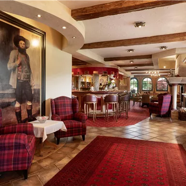 Ein gemütlicher Innenraum mit roten Sessel und einem großen Gemälde an der Wand. Im Hintergrund ist eine Bar mit Holzregalen und einem einladenden Ambiente zu sehen.