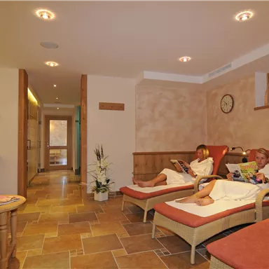 A quiet wellness area with comfortable loungers. Two people are relaxing in bathrobes and reading magazines.